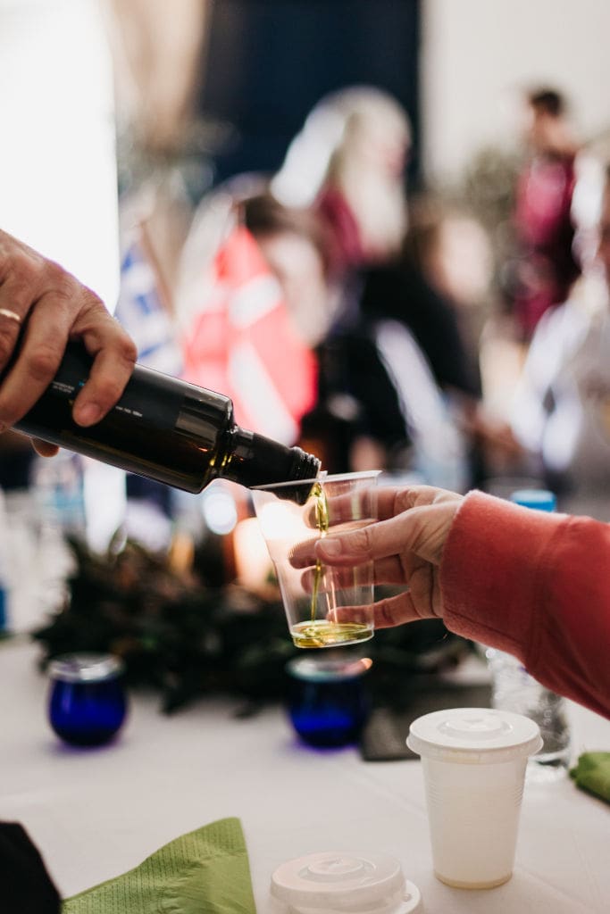 close-up of a man pouring olive oil in glass from the bottle at Konstas Olive Tours